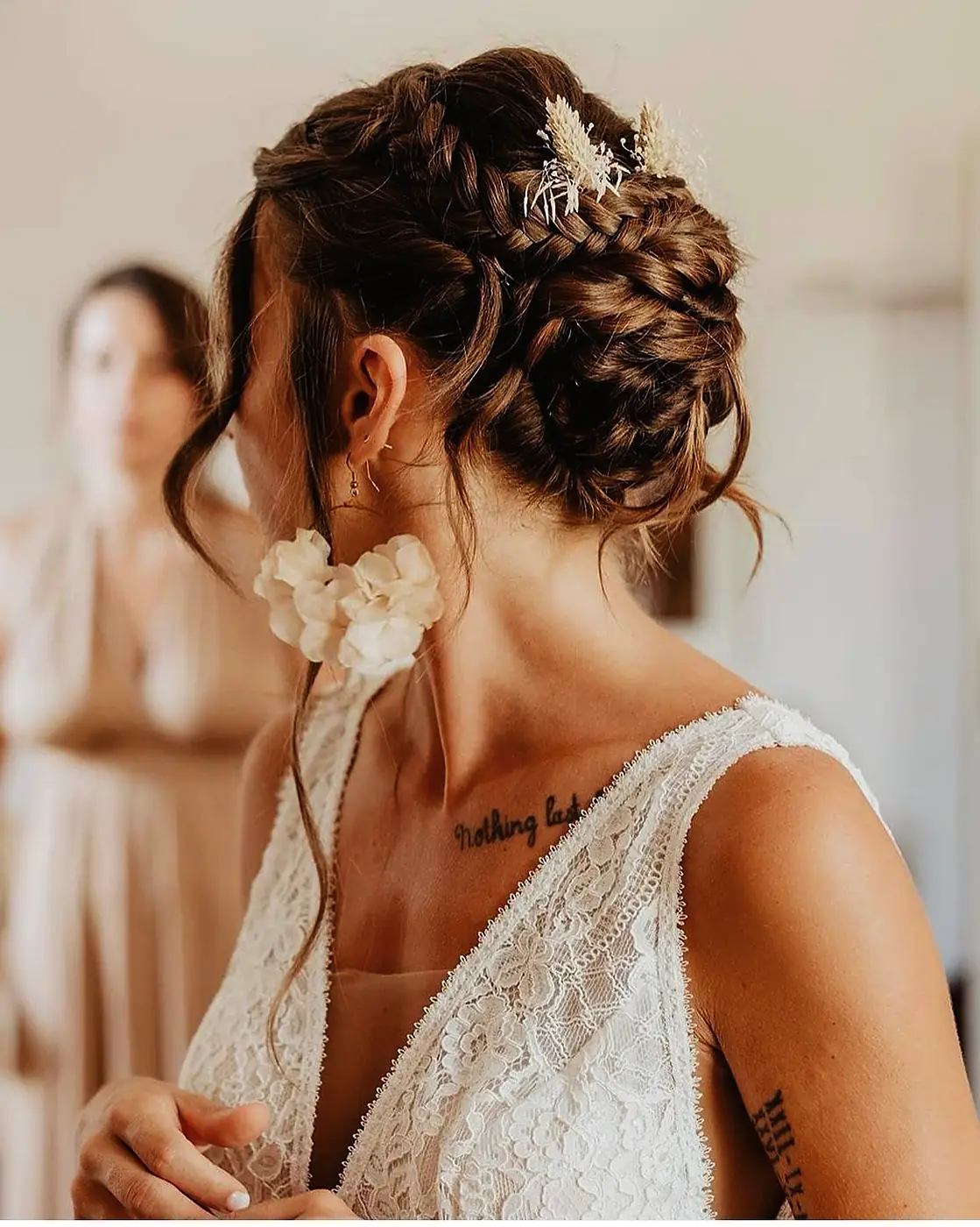 Chignon bohème tressé sur cheveux châtains orné d'épis de blé séchés, sur une mariée en robe de dentelle dos nu