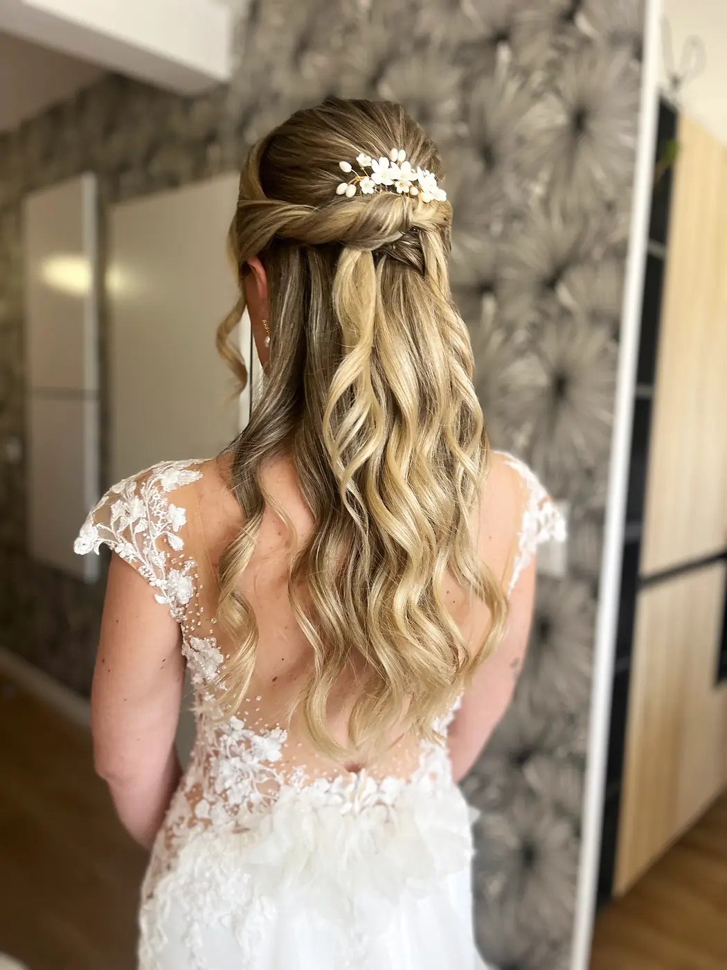 Demi-attache tressée sur un balayage blond ondulé, mariée en robe de dentelle dos nu